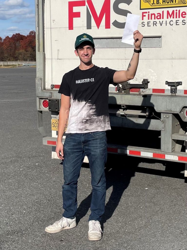 A man standing behind a large trailer holding up a piece of paper.