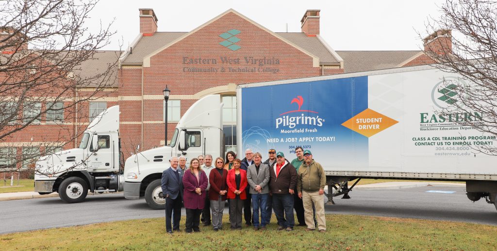 A group of people stand in front of a tractor-trailer.
