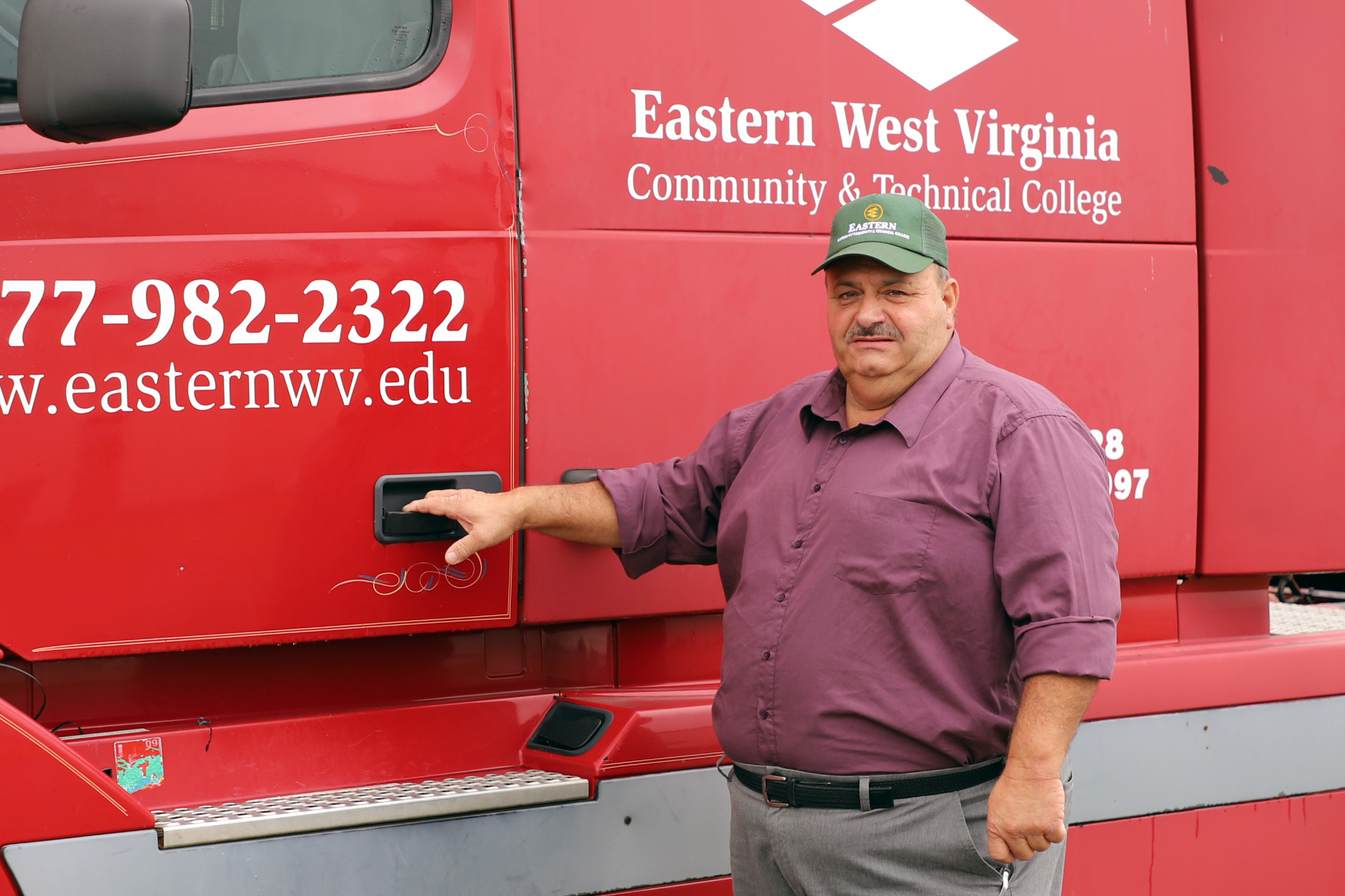 Man stands next to a large tractor trailer cab with his hand on the door handle of the truck.