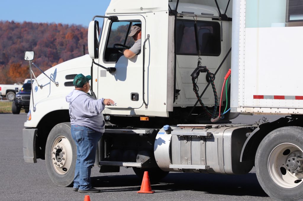 A man standing outside the driver's door of a large commercial truck talks with the driver of the truck.