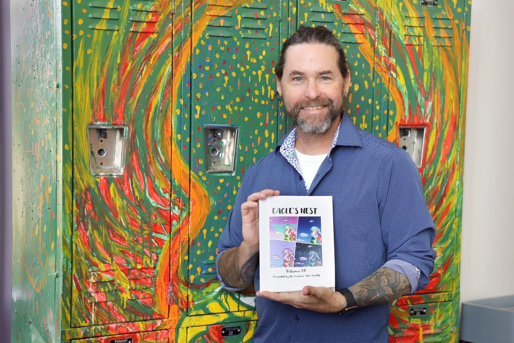 A man holds a copy of a booklet and shows the booklet's cover.